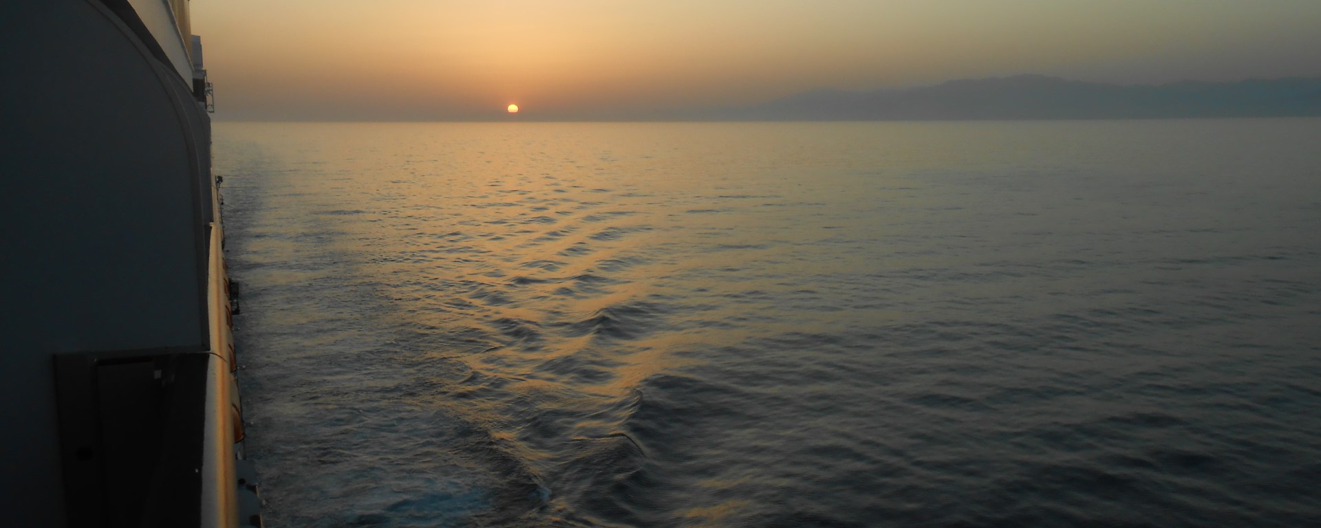 Sun setting from cruise ship balcony with ship's wake