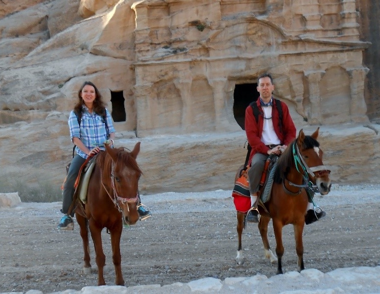 Man and woman on horseback in front of ancient stone tombs in Petra, Jordan