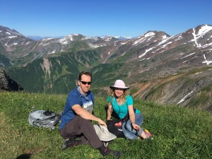 Couple seated atop a green mountain meadow on a clear day in Alaska
