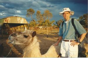 Man standing next to a seated camel in the Australian Outback