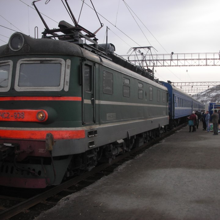 Dark green electric train locomotive pulling a passenger train in the Ural Mountains of Russia