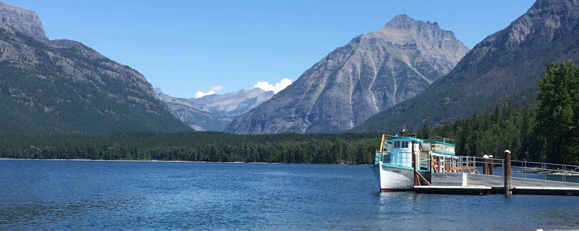 Classic boat on mountain lake framed by mountains on clear day in Glacier Park
