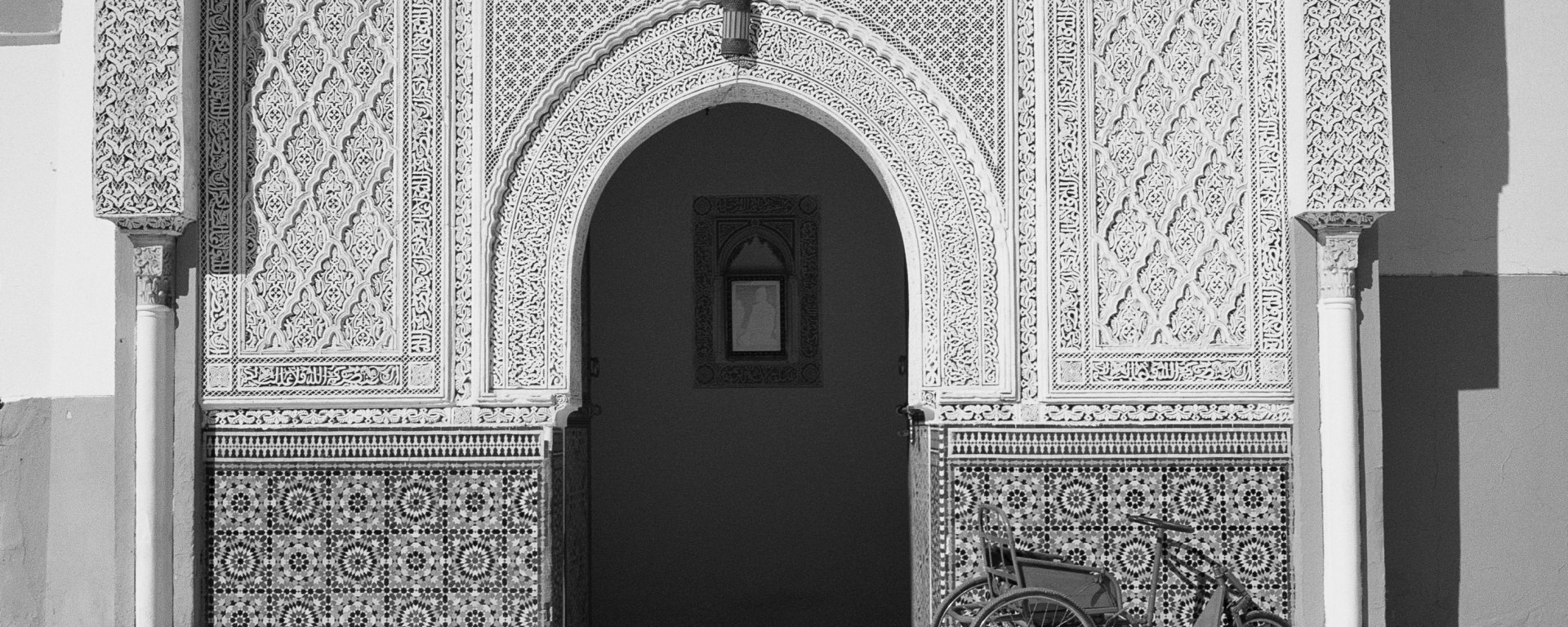 black and white photo of arched entrance in Morocco with old tricycle beside