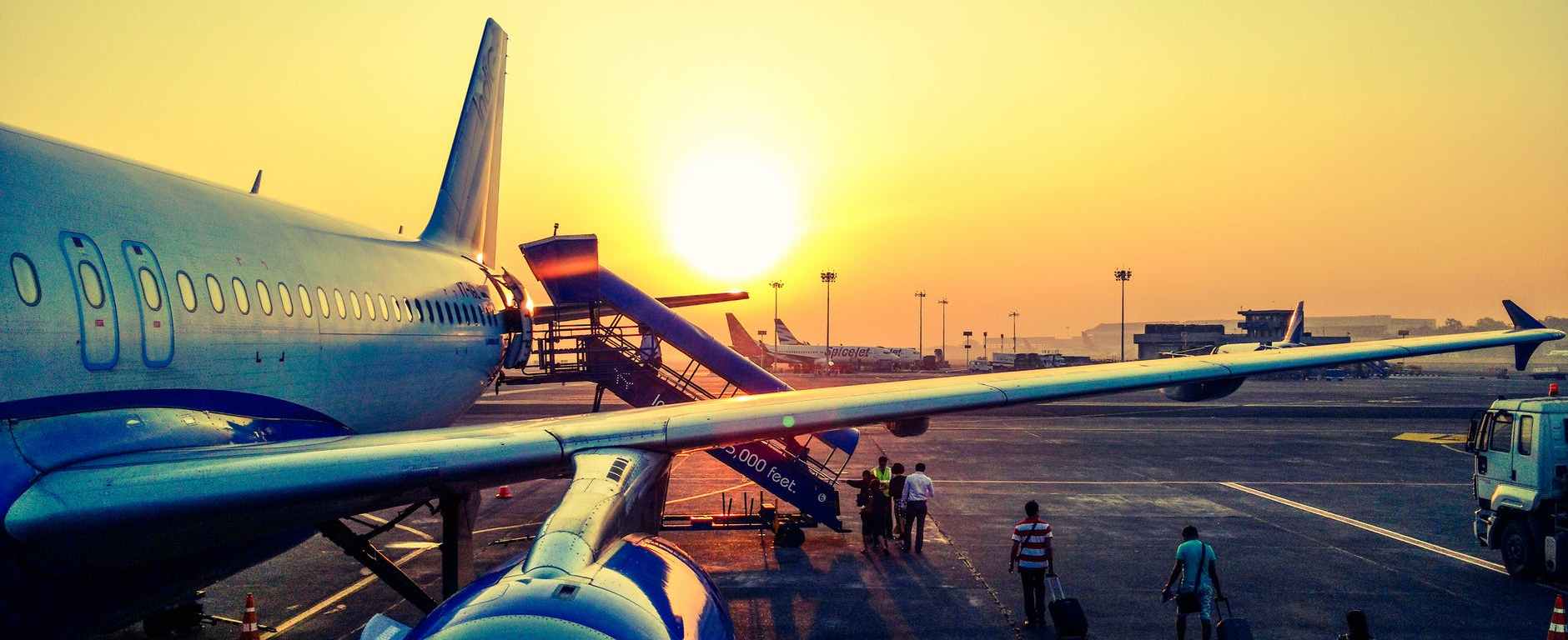 golden sunrise behind jet airplane with passengers boarding a stairway