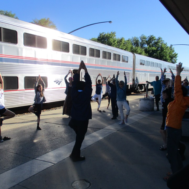 passengers doing a group morning stretch session on train platform with double-decker train cars in background