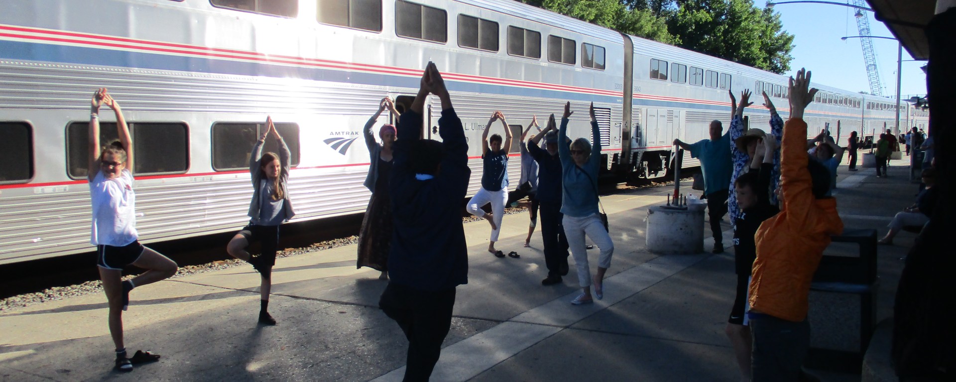 passengers doing a group morning stretch session on train platform with double-decker train cars in background