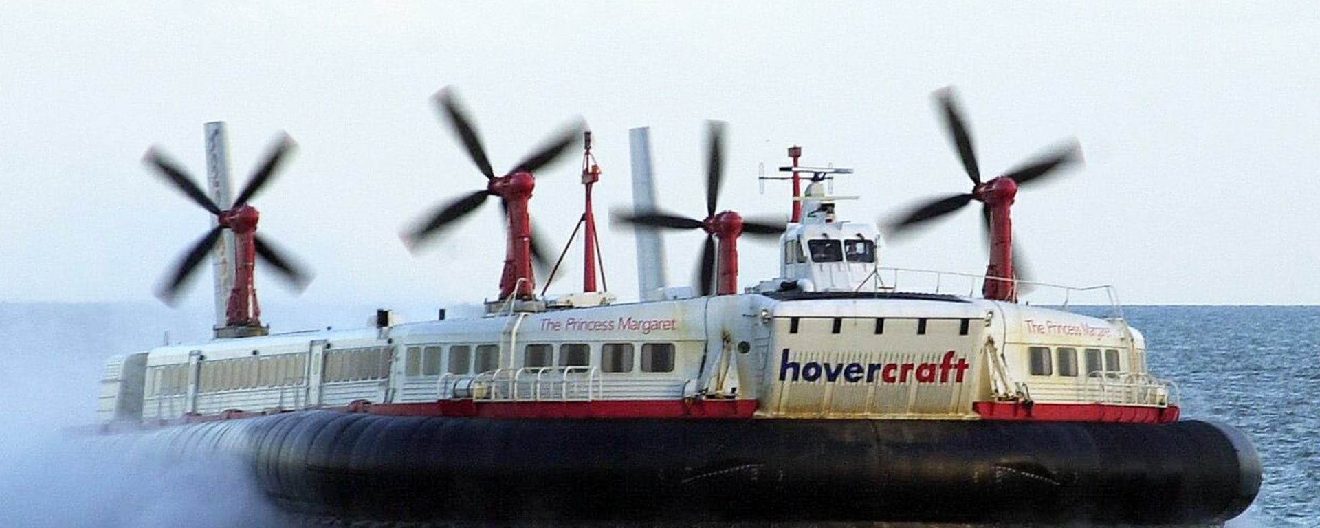 a giant passenger hovercraft speeds above the water with four huge propellers and a wraparound rubber skirt