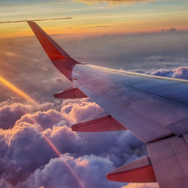 airplane wing above the clouds with golden sunshine rays
