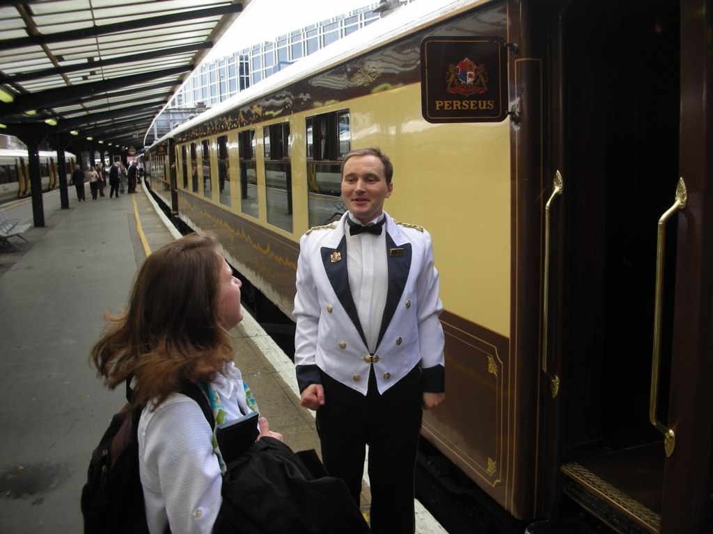 woman boarding train with white jacketed train steward